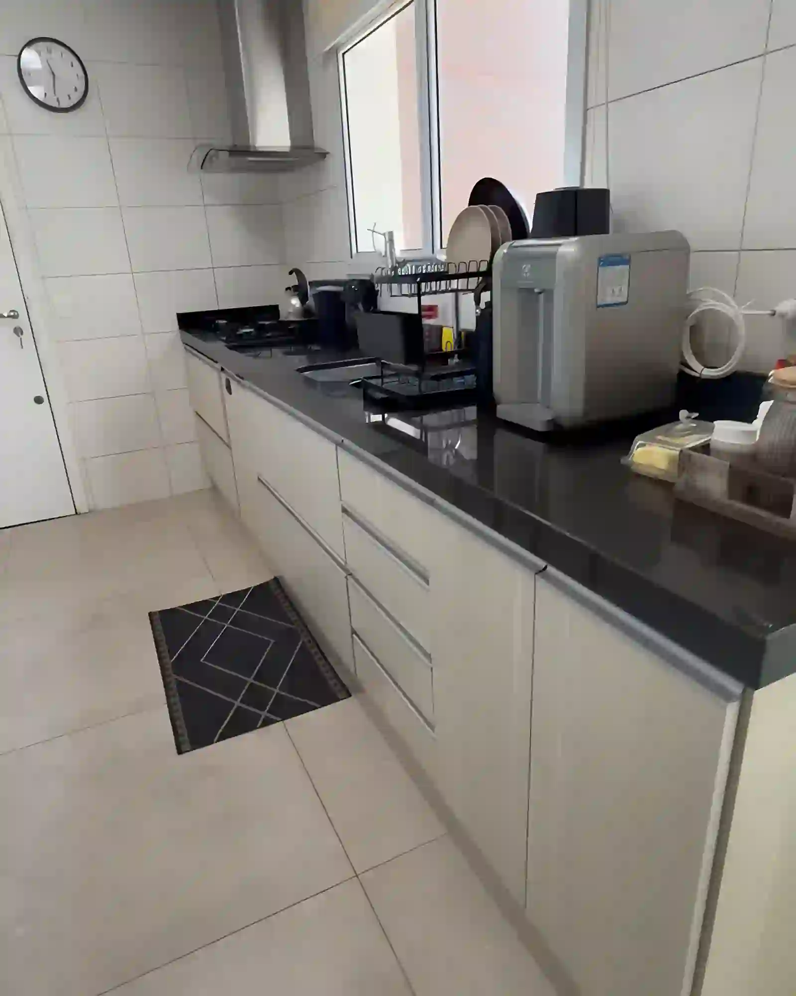 Cozinha planejada com bancada de granito preto, cooktop a gás e coifa de parede em inox, ao lado da janela.