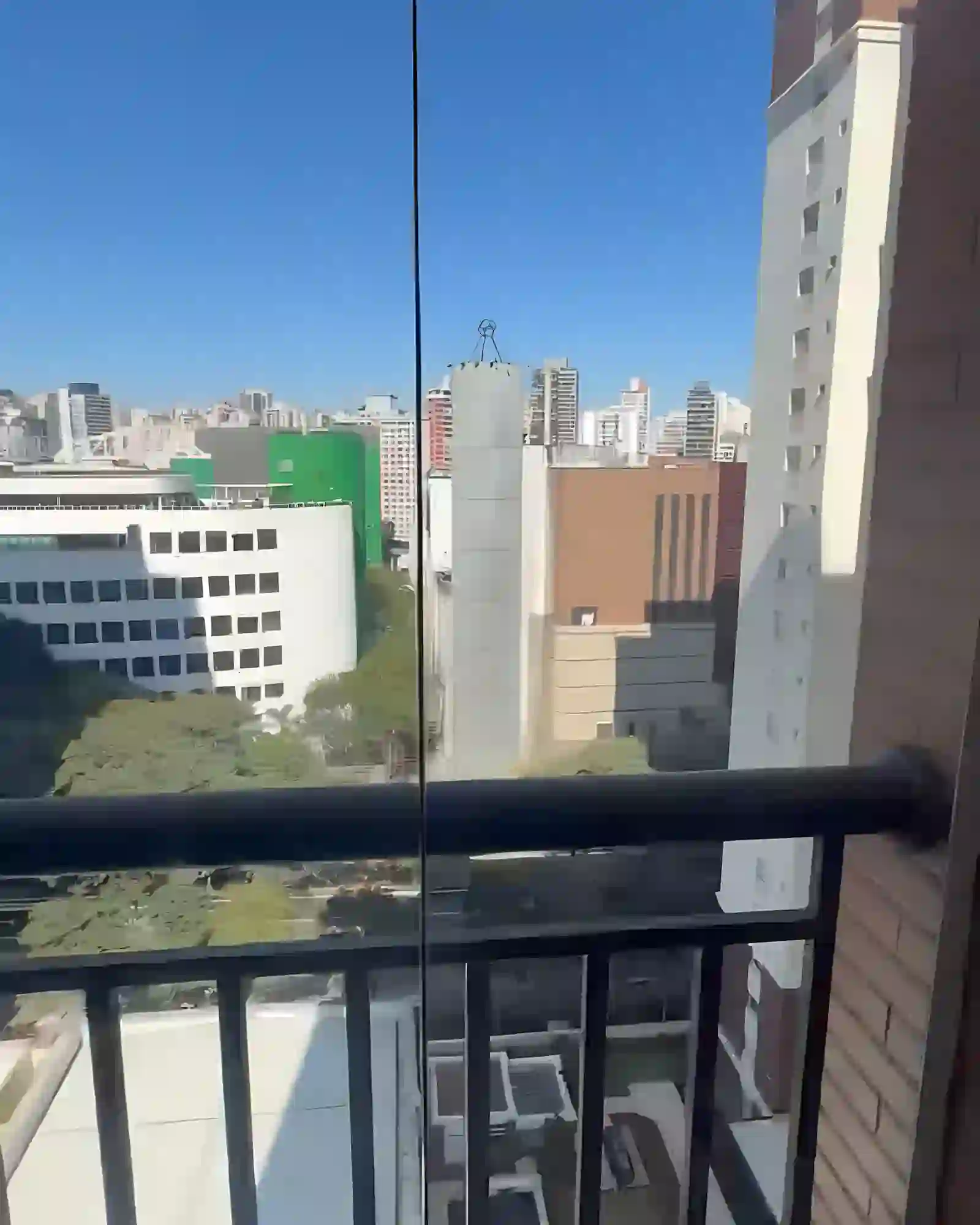 Vista da cidade a partir da varanda, com arborização da rua e prédios ao fundo.